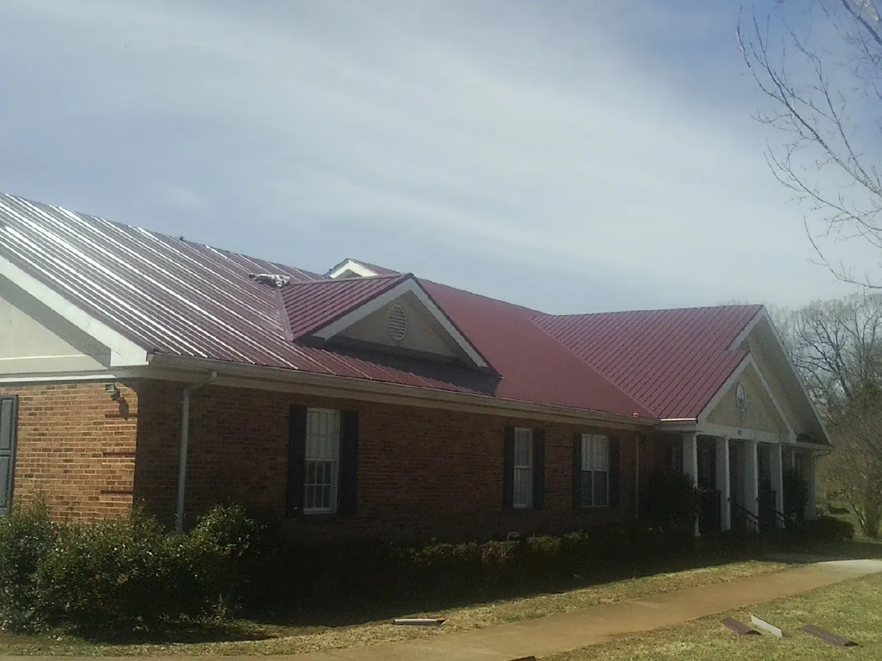 Red metal roof with gabled entries on a long brick building, from a Hail Damage Roof Repair job in Madrid
