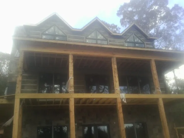 Dormers and porch framing on a large log home under construction — Roof Coating work by our crew in Madrid
